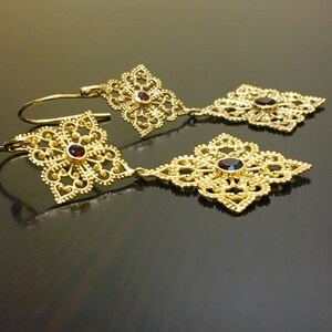 May include: Gold filigree earrings with red gemstone accents. The earrings feature a delicate, intricate design with a dangling drop.