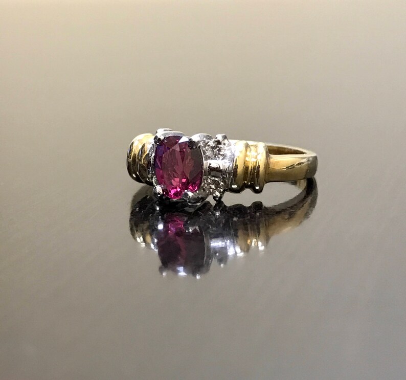 May include: A gold and silver ring with a large, oval-shaped, purple gemstone. The ring has a textured band.