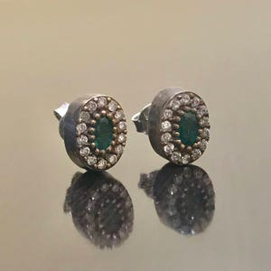 May include: A pair of silver earrings with a green oval gemstone surrounded by small white stones.