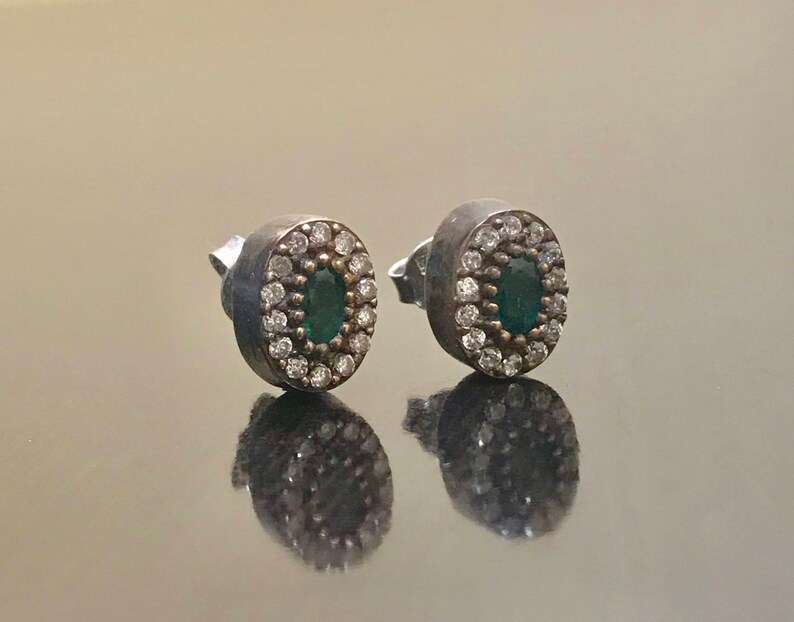 May include: A pair of silver earrings with a green oval gemstone surrounded by small white stones.