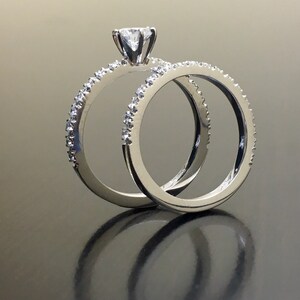 May include: A pair of silver wedding bands with a single diamond on the engagement ring. The rings are set with small diamonds around the band.