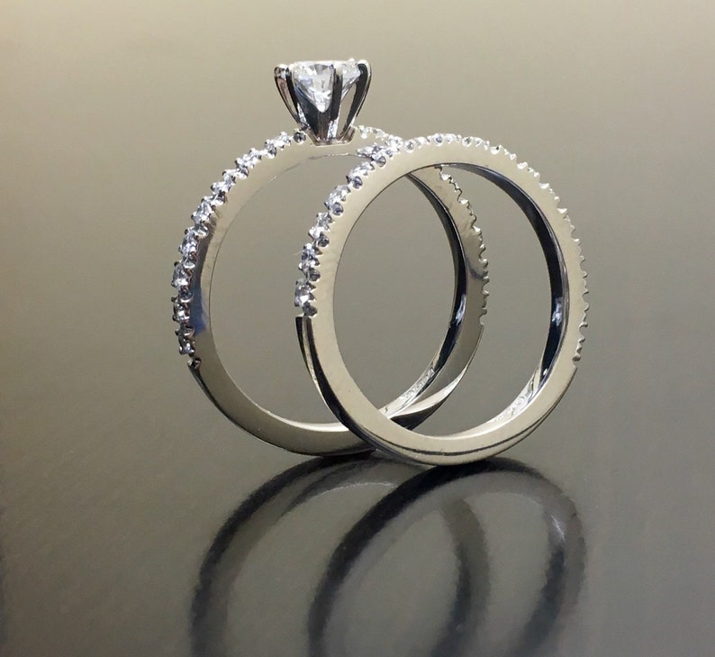 May include: A pair of silver wedding bands with a single diamond on the engagement ring. The rings are set with small diamonds around the band.