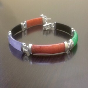 May include: A bracelet made of four different colored jade stones. The bracelet is silver and has a clasp. The stones are green, red, purple, and black.