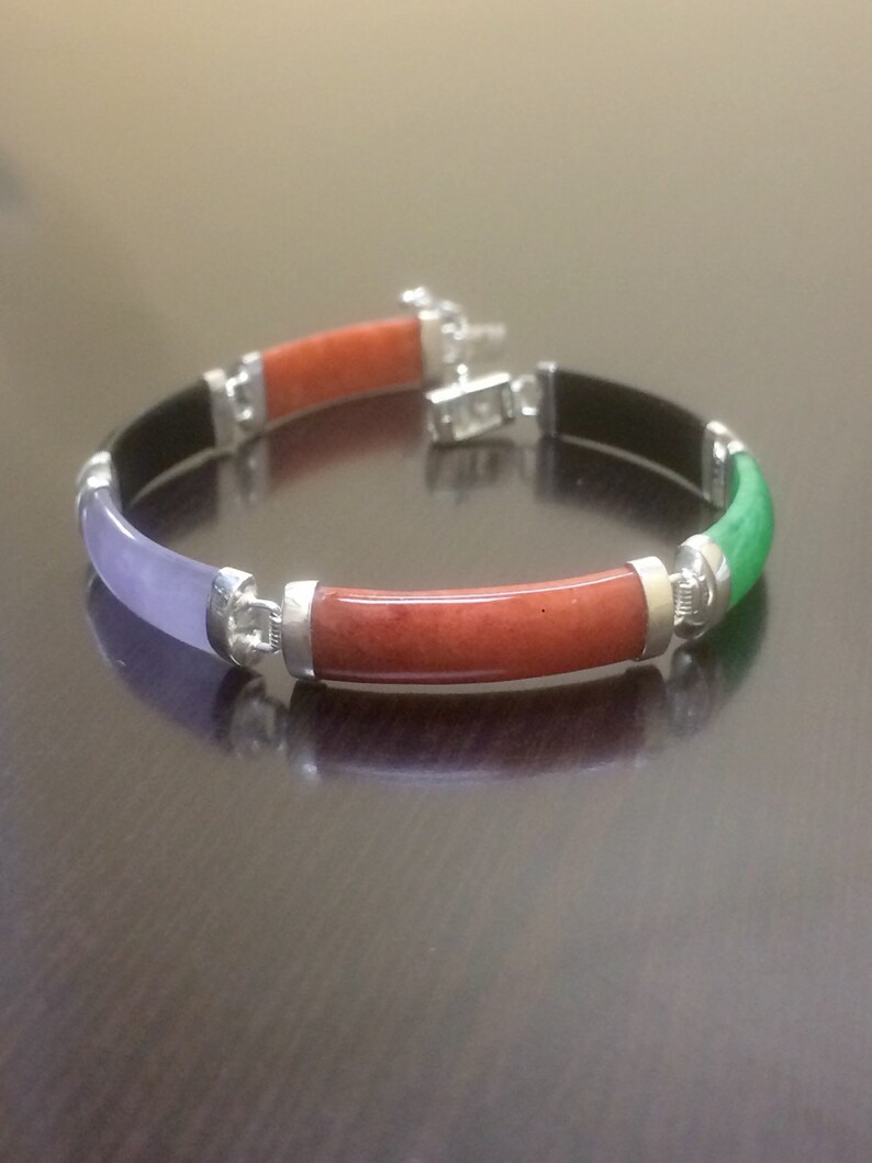 May include: A bracelet made of four different colored jade stones. The bracelet is silver and has a clasp. The stones are green, red, purple, and black.