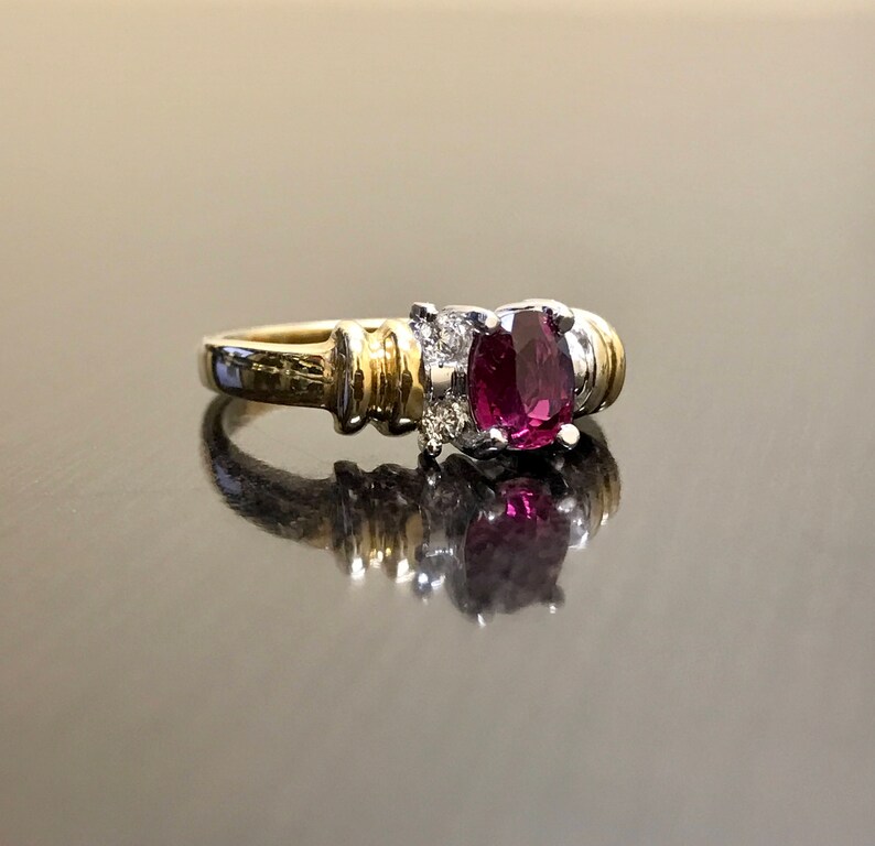 May include: A gold and silver ring with a large oval-shaped ruby gemstone surrounded by smaller diamonds.