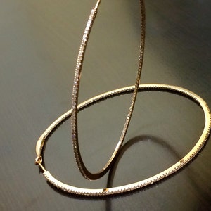 May include: A pair of gold hoop earrings with a row of small clear stones around the edge.