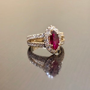 May include: A gold ring with a marquise-shaped ruby surrounded by a halo of smaller diamonds. The ring has a split shank with a row of diamonds on each side.