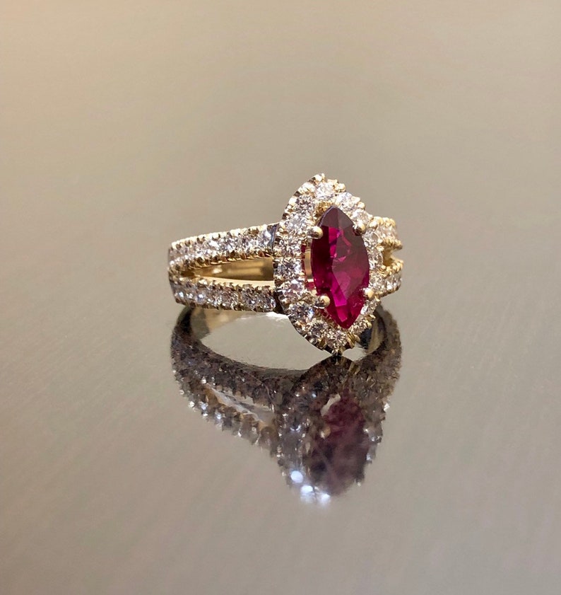 May include: A gold ring with a marquise-shaped ruby surrounded by a halo of smaller diamonds. The ring has a split shank with a row of diamonds on each side.