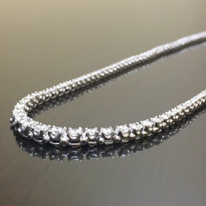 May include: A silver chain necklace with small, round, clear stones set in a prong setting. The necklace is laid out on a reflective surface.