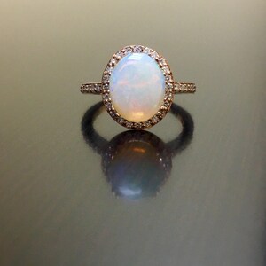May include: A rose gold ring with a large oval opal gemstone surrounded by a halo of smaller diamonds.
