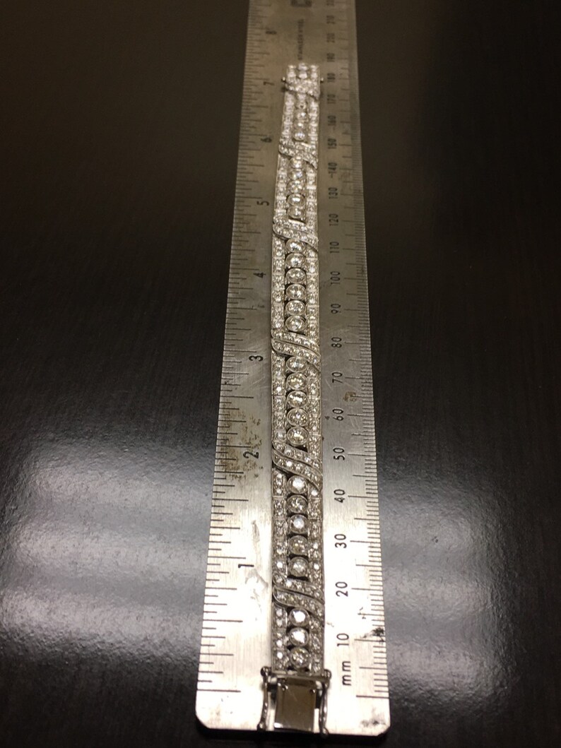 Puede incluir: Un brazalete de plata con una doble fila de diamantes redondos y una fila m&aacute;s peque&ntilde;a de diamantes pav&eacute;. El brazalete se mide con una regla, mostrando que tiene aproximadamente 6 cm de largo.