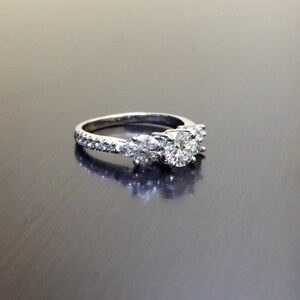 May include: A silver engagement ring with a large round centre diamond and smaller diamonds set in a pave setting around the band.