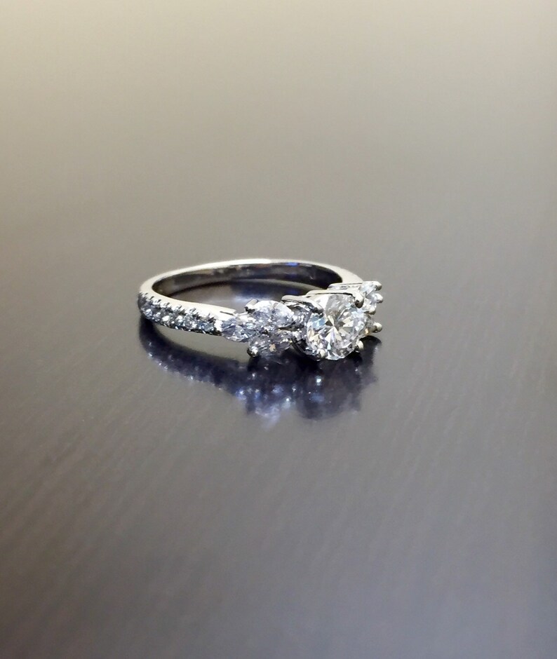 May include: A silver engagement ring with a large round centre diamond and smaller diamonds set in a pave setting around the band.