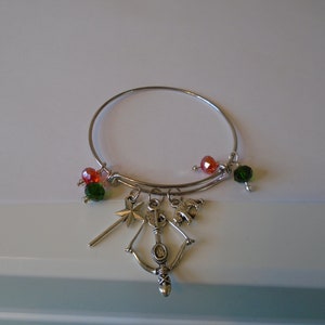 May include: A silver bangle bracelet with charms, including a star, a bow and arrow, and a lion. The bracelet is decorated with red and green beads.