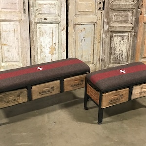 Puede incluir: Dos bancos de madera con patas de metal y cojines de tela a rayas rojas y marrones. Los bancos tienen tres cajones cada uno, etiquetados como "Churchills 69" y presentan una cruz blanca en los cojines.