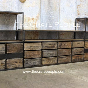 May include: A black metal shelving unit with wooden crates used as drawers. The crates are labeled with various company names and locations. The unit has three shelves and is made of sturdy metal. The shelves are adjustable and can be used to store a variety of items. The unit is perfect for adding a rustic and industrial touch to any room.