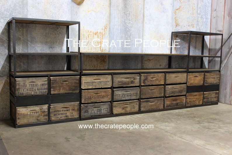 May include: A black metal shelving unit with wooden crates used as drawers. The crates are labeled with various company names and locations. The unit has three shelves and is made of sturdy metal. The shelves are adjustable and can be used to store a variety of items. The unit is perfect for adding a rustic and industrial touch to any room.