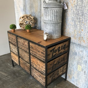 May include: A black metal frame dresser with six drawers made from reclaimed wood crates. The drawers are labeled with the text "Zoria Farms, Inc." and "Brentwood & Madera, San Jose, CA 1993".