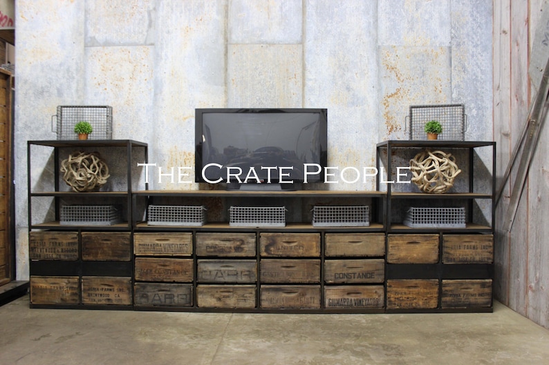 May include: A black metal media console with wooden drawers. The drawers are labeled with various words, including "Constance" and "Barbara Vineyards". The console has two shelves on each side, with a black metal frame and a wooden top. A flat screen TV is mounted on the top shelf. There are two small potted plants on the shelves.