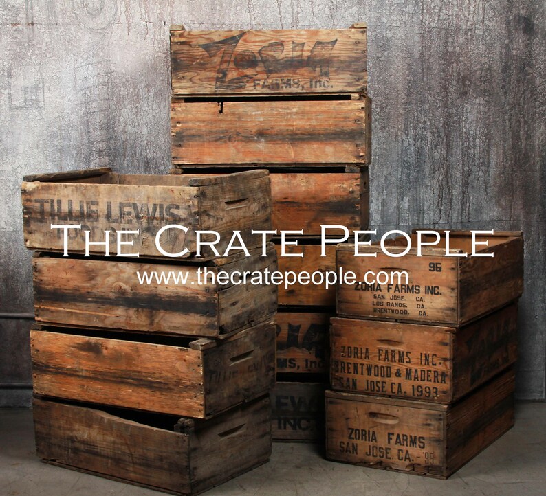 May include: A stack of vintage wooden crates with various labels and markings. The crates are made of weathered wood and have a rustic appearance. The labels include the text "Zoria Farms Inc." and "Tillie Lewis".