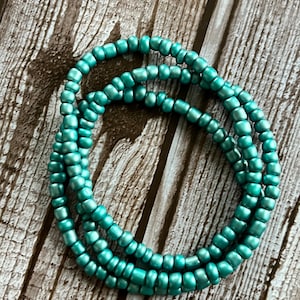 May include: A set of teal blue glass beads strung together in a circle. The beads are small and have a metallic sheen.