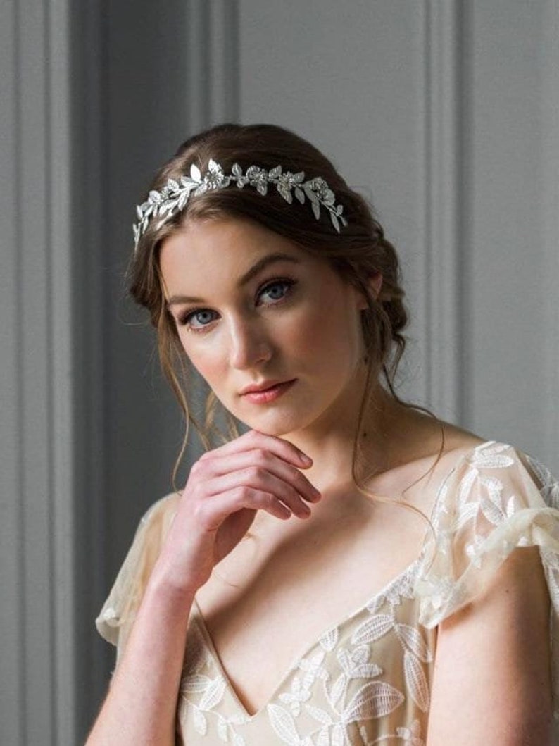 May include: A woman wearing a white lace dress with a silver floral crown in her hair.