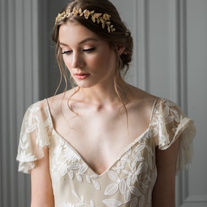May include: A woman wearing a beige dress with white floral embroidery and a gold leaf and flower crown.