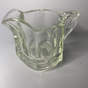 Peut inclure: Une crémière en verre transparent avec un design géométrique décoratif. La crémière a une poignée et un bec verseur pour faciliter le versement. Le verre est légèrement teinté et la crémière a une esthétique vintage.