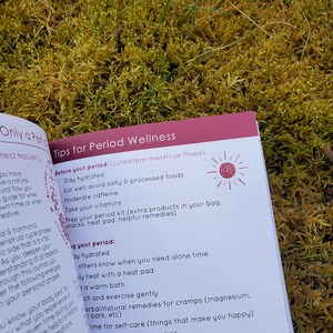 May include: A pink and white booklet with the title "Tips for Period Wellness" and a list of tips for managing your period. The booklet is open to a page with the heading "Before your period: (Luteal/pre-menstrual Phase)" and a list of tips for staying hydrated, eating well, and preparing for your period.