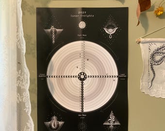 Könnte beinhalten: Ein schwarz-weißer 2027 "lunar insights" Wandkalender mit einem zentralen kreisförmigen Diagramm der Mondphasen, umgeben von saisonalen botanischen Illustrationen in den Ecken und dem Text "let the cycles be your guide" am unteren Rand.