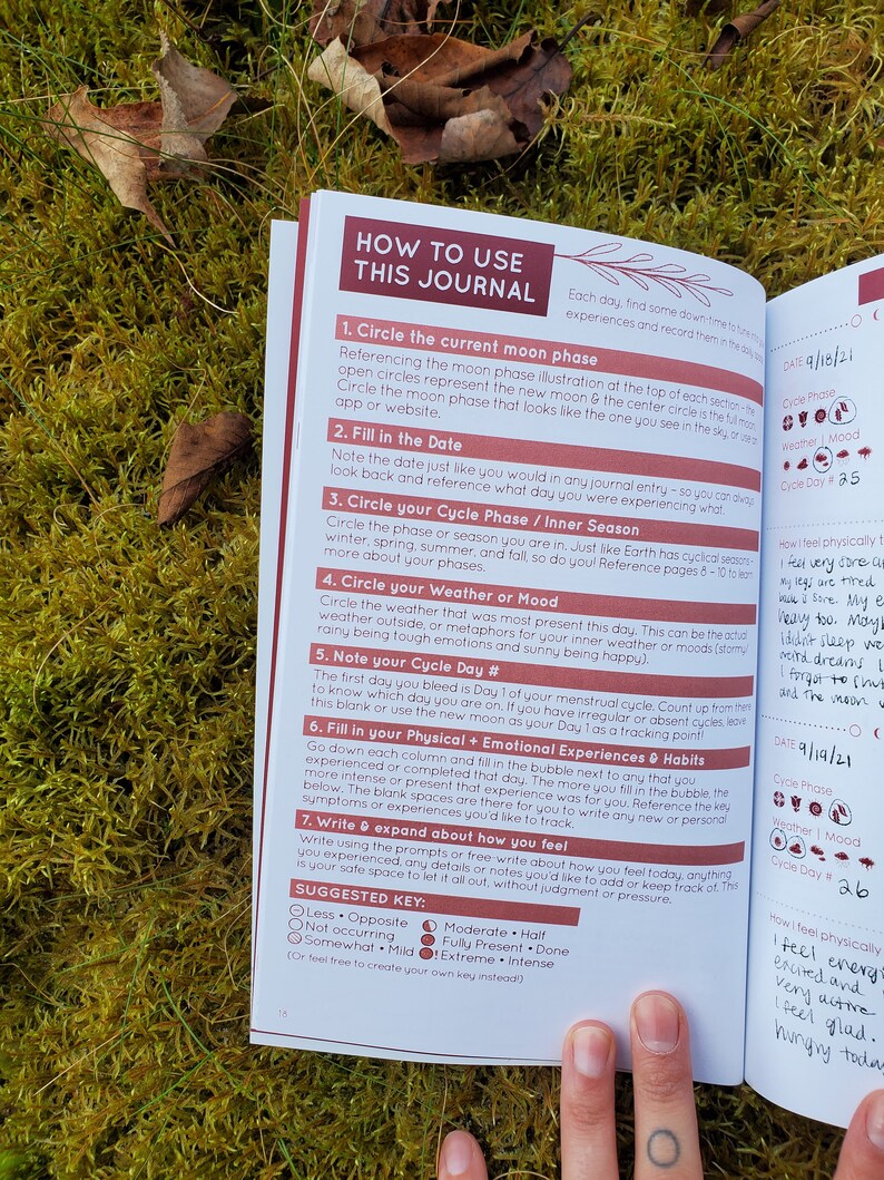 May include: A close-up of a journal with a pink and red cover. The journal is open to a page with instructions on how to use the journal. The page includes a section on tracking your menstrual cycle, mood, and physical and emotional experiences.