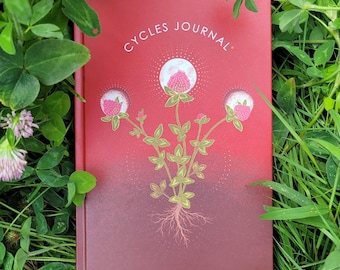 Könnte beinhalten: Ein rotes Hardcover-Notizbuch mit dem in Weiß gedruckten Text Cycles Journal. Der Einband zeigt eine goldfarbene Illustration einer Kleepflanze mit drei rosa Blütenköpfen, die jeweils von einem weißen Mondkreis umgeben sind.
