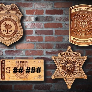 May include: Four wooden plaques featuring law enforcement emblems. Top left: South Carolina Agent badge. Top right: El Paso County Sheriff's Office SRT shield. Bottom left: Illinois Sheriff license plate. Bottom right: California State Park star badge.