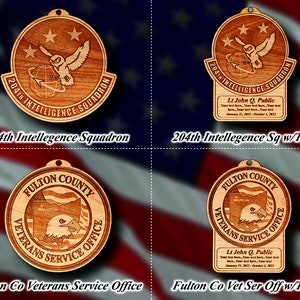 May include: Four wooden ornaments with a circular design. The top left ornament features a white owl with a globe and the text "204th Intelligence Squadron". The top right ornament features the same owl and globe with the text "204th Intelligence Squadron" and a personalized text box below. The bottom left ornament features a bald eagle with the text "Fulton County Veterans Service Office". The bottom right ornament features the same eagle with the text "Fulton County Veterans Service Office" and a personalized text box below.