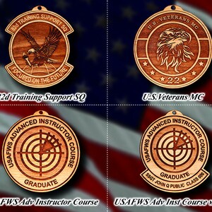 May include: Four wooden ornaments with different designs. The top left ornament is a round, brown wooden plaque with the text "82d Training Support SQ" and an eagle design. The top right ornament is a round, brown wooden plaque with the text "U.S. Veterans MC" and an eagle design. The bottom left ornament is a round, brown wooden plaque with the text "USAFWS Advanced Instructor Course" and a target design. The bottom right ornament is a round, brown wooden plaque with the text "USAFWS Advanced Instructor Course" and a target design, along with the text "SSGT JOHN Q PUBLIC CLASS 000".