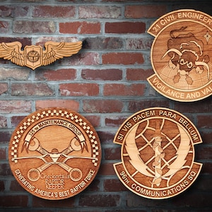 May include: Four wooden plaques with engraved designs and text. The top plaque reads "21 CIVIL ENGINEER SQ VIGILANCE AND VALOR". The plaque below it reads "SI VIS PACEM PARA BELLUM 96TH COMMUNICATIONS SQ". The plaque on the left reads "325TH MAINTENANCE GROUP GENERATING AMERICA'S BEST RAPTOR FORCE Checkertails RAPTOR KEEPER".