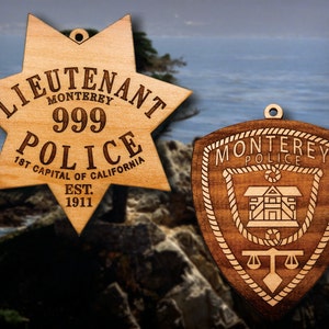 May include: Two wooden ornaments shaped like a star and a shield. The star ornament has the text "Lieutenant Monterey Police 999 1st Capital of California Est. 1911". The shield ornament has the text "Monterey Police".