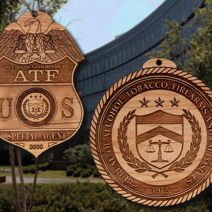 May include: Two wooden ornaments featuring the ATF logo. The first ornament is a shield with the text "DEPARTMENT OF JUSTICE ATF US SPECIAL AGENT 0000". The second ornament is a round seal with the text "BUREAU OF ALCOHOL, TOBACCO, FIREARMS AND EXPLOSIVES 1972".