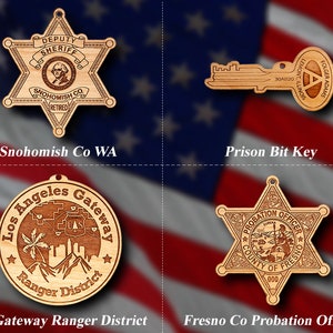May include: Four wooden ornaments featuring law enforcement and government themes. The first is a star-shaped sheriff's badge with the text "DEPUTY SHERIFF SNOHOMISH CO RETIRED". The second is a key with the text "FOLGER ADAMS LEMONT ILLINOIS 30AB20". The third is a round ornament with the text "Los Angeles Gateway Ranger District". The fourth is a star-shaped ornament with the text "PROBATION OFFICER COUNTY OF FRESNO 000".