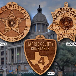May include: Three wooden ornaments featuring the Harris County Constable logo. The first ornament is a round badge with a star and the text "DEPUTY PRECINCT 4 HARRIS CO. CONSTABLE". The second ornament is a six-pointed star badge with the text "MAJOR HARRIS COUNTY CONSTABLE STATE OF TEXAS PRECINCT 3". The third ornament is a shield-shaped patch with the text "HARRIS COUNTY CONSTABLE" and the number "4" inside the outline of the state of Texas.