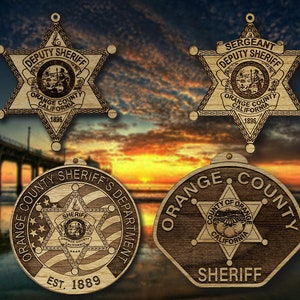 May include: Four wooden ornaments shaped like sheriff's badges. The top two ornaments are five-pointed stars with the text "DEPUTY SHERIFF" and "SERGEANT DEPUTY SHERIFF". The bottom two ornaments are round with the text "ORANGE COUNTY SHERIFF'S DEPARTMENT" and "ORANGE COUNTY SHERIFF".