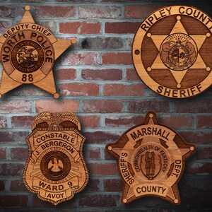 May include: Four wooden law enforcement badges with different designs. The top left badge is a five-pointed star with the text "Deputy Chief Worth Police" and "State of Illinois 88". The top right badge is a five-pointed star with the text "Ripley County Sheriff". The bottom left badge is a shield with the text "Constable J. Bergeron Ward 9 Avoy". The bottom right badge is a five-pointed star with the text "Sheriff's Marshall County Dept."