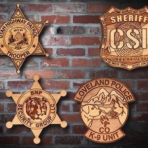 May include: Four wooden plaques with different law enforcement and security logos. The top left plaque is a star-shaped badge with the text "Utah Highway Patrol" and "Trooper". The top right plaque is a shield-shaped badge with the text "Sheriff CSI Ocean County". The bottom left plaque is a star-shaped badge with the text "BNP Security Group LLC". The bottom right plaque is a rounded badge with the text "Loveland Police CO K-9 Unit".