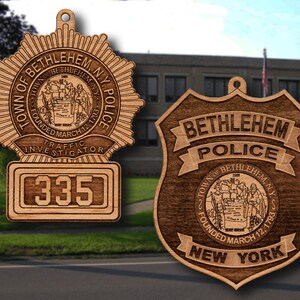 May include: Two wooden ornaments shaped like police badges. The first badge is a star-shaped badge with the text "Town of Bethlehem, N.Y. Police" and "Founded March 12, 1793". The second badge is a shield-shaped badge with the text "Bethlehem Police" and "Town of Bethlehem, N.Y. Founded March 12, 1793".