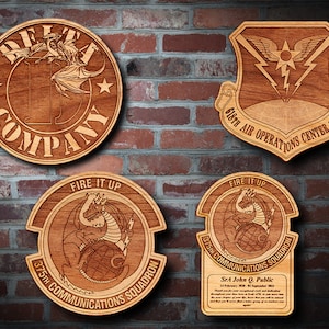 May include: Four wooden plaques with laser-engraved designs. The top left plaque is round and features a dragon with the text "DEFI COMPANY". The top right plaque is shaped like a shield and features a lightning bolt with the text "618TH AIR OPERATIONS CENTER (TACO)". The bottom left plaque is round and features a dragon with the text "FIRE IT UP 375TH COMMUNICATIONS SQUADRON". The bottom right plaque is rectangular and features a dragon with the text "FIRE IT UP 375TH COMMUNICATIONS SQUADRON" and a thank you message for "SrA John Q. Public".