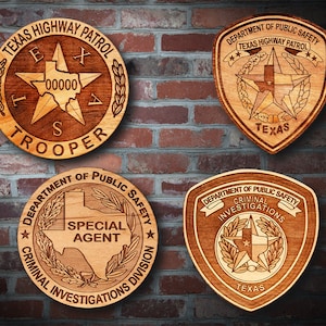 Könnte beinhalten: Vier Holzplaketten mit dem Logo der Texas Highway Patrol. Die obere linke Plakette zeigt "Texas Highway Patrol" und "Trooper" mit einem Stern und dem Bundesstaat Texas im Inneren. Die obere rechte Plakette zeigt "Department of Public Safety" und "Texas Highway Patrol" mit einem Stern und dem Bundesstaat Texas im Inneren. Die untere linke Plakette zeigt "Department of Public Safety" und "Criminal Investigations Division" mit einem Stern und dem Bundesstaat Texas im Inneren. Die untere rechte Plakette zeigt "Department of Public Safety" und "Criminal Investigations" mit einem Stern und dem Bundesstaat Texas im Inneren.