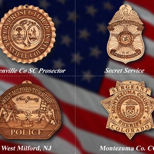 Könnte beinhalten: Vier Holzornamente mit Abzeichen von Strafverfolgungsbehörden. Das Ornament oben links ist ein rundes Abzeichen mit dem Text "PROSECTOR GREENVILLE COUNTY SC". Das Ornament oben rechts ist ein schildförmiges Abzeichen mit dem Text "US SECRET SERVICE SPECIAL AGENT". Das Ornament unten links ist ein sechseckiges Abzeichen mit dem Text "WEST MILFORD TOWNSHIP NEW JERSEY POLICE 1834". Das Ornament unten rechts ist ein sechszackiger Stern mit dem Text "SERGEANT MONTEZUMA COUNTY STATE OF COLORADO SHERIFF COLORADO".