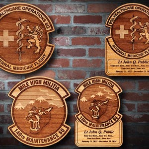 May include: Three wooden plaques with engraved designs. The top plaque is brown with a white cross, a snake wrapped around a sword, and a lion. The text reads "96th HEALTHCARE OPERATIONS SQ INTERNAL MEDICINE FLIGHT". The middle plaque is brown with a mountain range, a panther, and the text "MILE HIGH MILITIA 140TH MAINTENANCE SQ". The bottom plaque is brown with a mountain range, a panther, and the text "MILE HIGH MILITIA 140TH MAINTENANCE SQ".