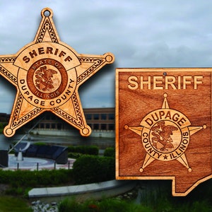 May include: Two wooden sheriff's star badges. The first badge is a five-pointed star with the words "Sheriff", "State of Illinois", "DuPage County" around the perimeter. The second badge is a square with the word "Sheriff" at the top and a five-pointed star with the words "DuPage County Illinois" around the perimeter.