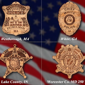 May include: Four wooden ornaments shaped like police badges. The top left ornament is a Westborough, Massachusetts police badge with the text "Westborough, MA". The top right ornament is a Chief White, Georgia police badge with the text "White, GA". The bottom left ornament is a Lake County, Indiana sheriff's badge with the text "Lake County, IN". The bottom right ornament is a Worcester County, Maryland sheriff's badge with the text "Worcester Co. MD 250 Year".